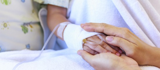 Close-up of a parent holding a tiny, bandaged newborn hand in a hospital bed with an IV line nearby.