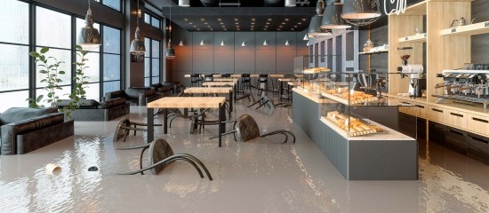 Flooded cafe interior with water covering the floor, chairs partly submerged, and a bakery counter to the right.