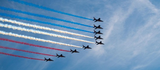 Nine jets in tight formation streaming red, white, and blue smoke across a clear blue sky, performing an air show.