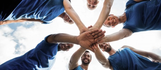 Group of people in blue shirts joining hands in a circle outdoors to show teamwork and unity.