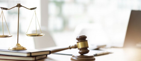 Scales of justice and a wooden gavel resting on legal books on a desk, with a blurred office background.