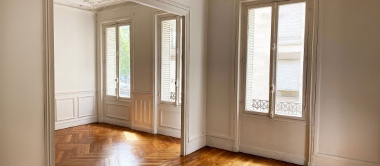 k4_24711721 Bright empty room with large windows, white paneled walls, and herringbone wooden floor letting in sunlight.