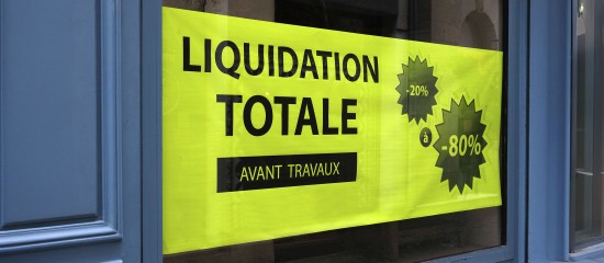 k4_24723640 Bright yellow sale sign in a blue storefront window reading 'LIQUIDATION TOTALE' with 'AVANT TRAVAUX' and starburst discount graphics showing 20% and up to 80%.
