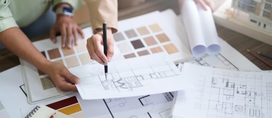 Two designers review color swatches and architectural plans on a table, with drafts and rolled blueprints nearby.
