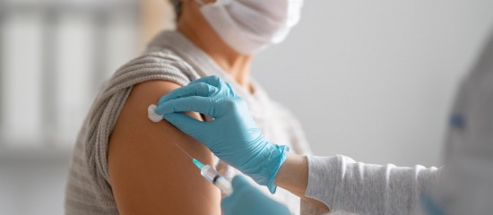 Healthcare worker wearing gloves administers a vaccination to a patient’s upper arm while masking in a clinical setting