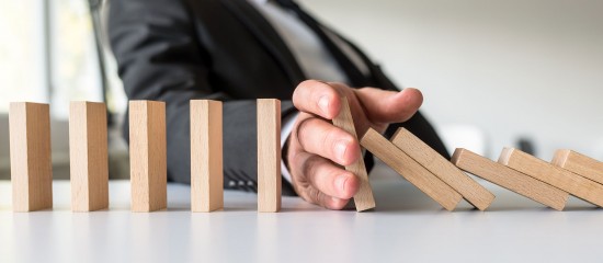 Hand in a suit stopping a row of wooden domino blocks from toppling.
