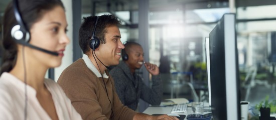 Three call-center agents wearing headsets work at computer desks in a busy office.