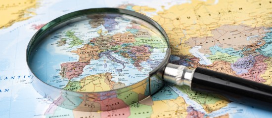 Magnifying glass over a colorful world map, focusing on Europe, suggesting close geographic study.