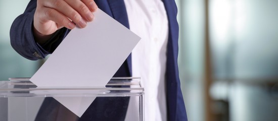 Person in a suit places a ballot into a transparent ballot box.